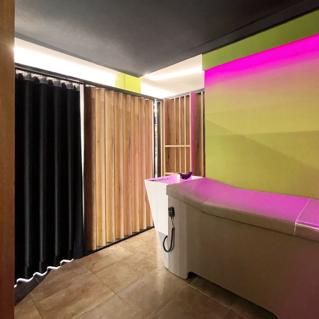 Interno della Tricoroom con vista sul lettino e lavatesta. Colori neutri e luci Led decorative rosa 